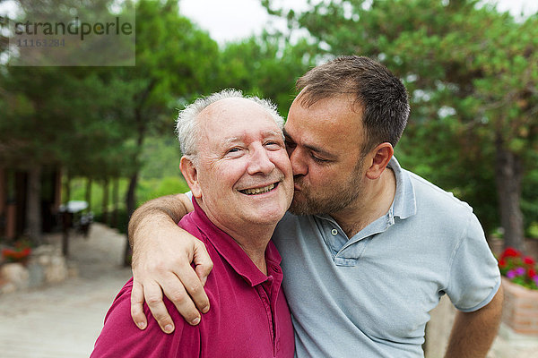 Ein erwachsener Sohn  der seinen alten Vater küsst und umarmt.