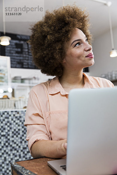 Lächelnde junge Frau mit Laptop in einem Café  die nach oben schaut.