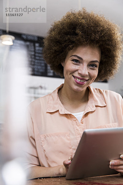 Lächelnde junge Frau mit digitalem Tablett in einem Cafe