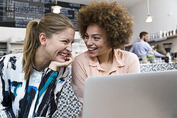 Zwei glückliche junge Frauen mit Laptop in einem Cafe