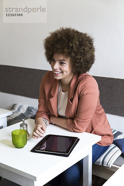 Lächelnde junge Frau mit digitalem Tablett im Cafe