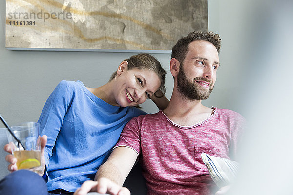 Lächelndes junges Paar auf der Couch sitzend mit Getränk