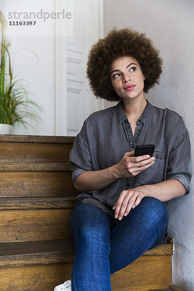 Junge Frau sitzt auf einer Treppe und hält ein Smartphone.