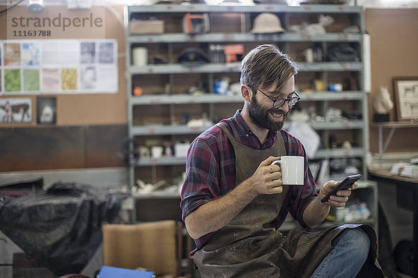 Mann mit Handy bei Kaffeepause in der Werkstatt