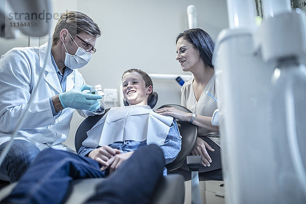 Kieferorthopäde erklärt dem Jungen mit der Mutter in der Zahnarztpraxis die Zahnform.