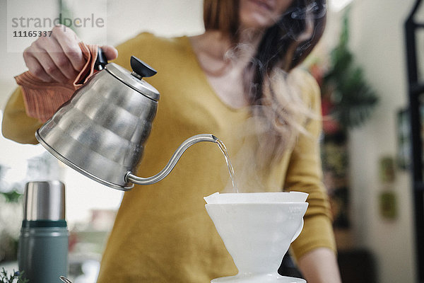 Eine Frau schüttet Kaffee aus einer Kanne durch einen Papierfilter.