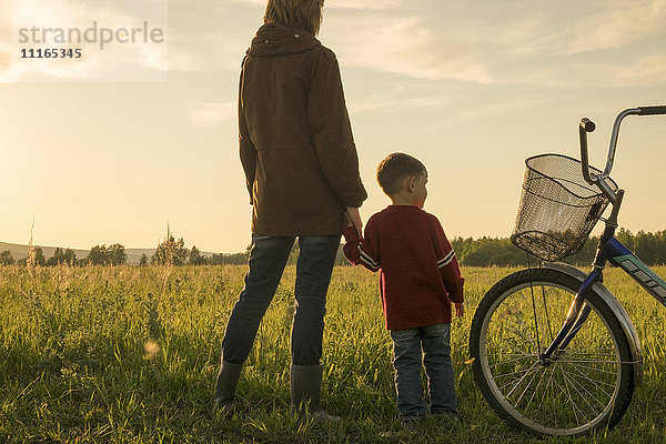 Mutter und Sohn halten sich auf einem Feld in der Nähe eines Fahrrads an den Händen