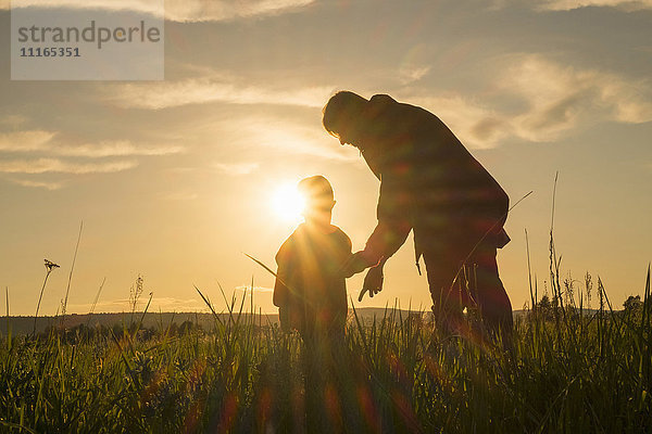 Frau und Sohn stehen bei Sonnenuntergang auf einem Feld