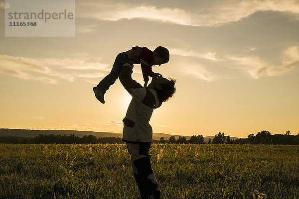 Mari Mann hebt Sohn im Feld bei Sonnenuntergang