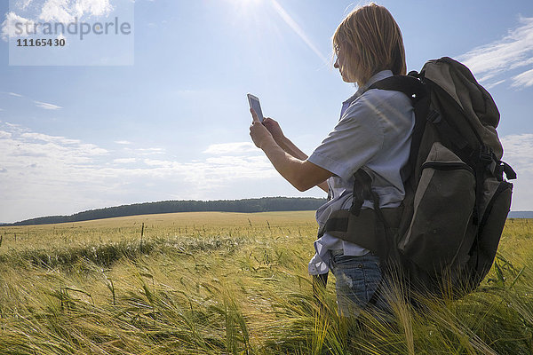 Kaukasische Frau steht auf einem Feld und benutzt ein Mobiltelefon