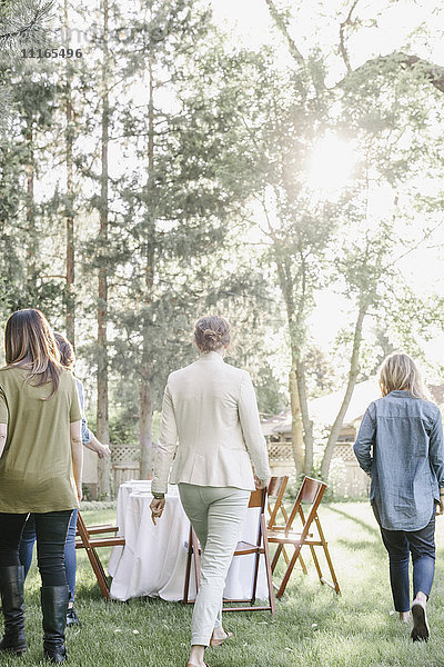 Drei Frauen gehen auf einen Tisch und Stühle in einem Garten zu.