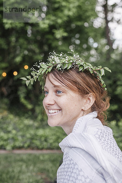 Lächelnde Frau mit einem Blumenkranz im Haar  die in einem Garten sitzt.