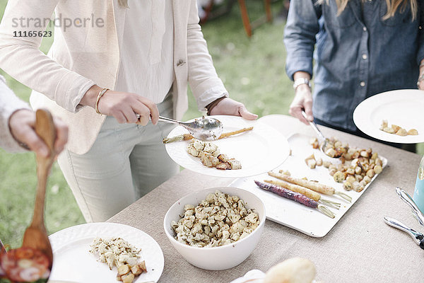 Teller und Schüsseln mit Essen auf einem Tisch bei einer Gartenparty.