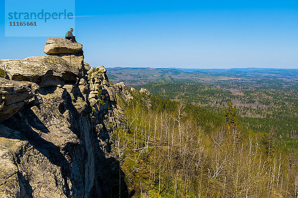 Kaukasischer Mann sitzt auf einem Bergfelsen und bewundert die malerische Aussicht