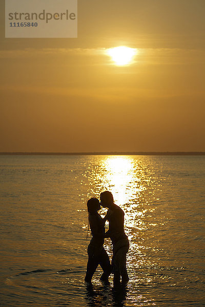 Silhouette eines kaukasischen Paares  das sich bei Sonnenuntergang im Meer küsst