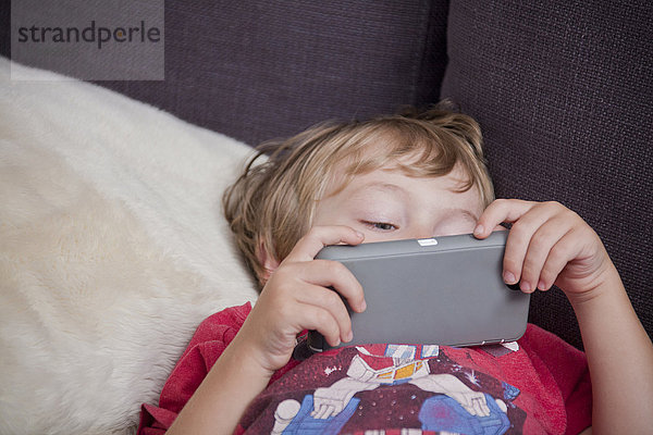 Kaukasischer Junge liegt auf dem Sofa und schaut auf sein Handy