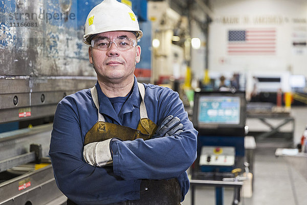 Ernster hispanischer Arbeiter  der in einer Fabrik posiert