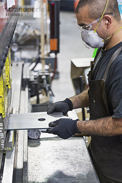 Hispanischer Arbeiter mit Maske bei der Metallverarbeitung in einer Fabrik