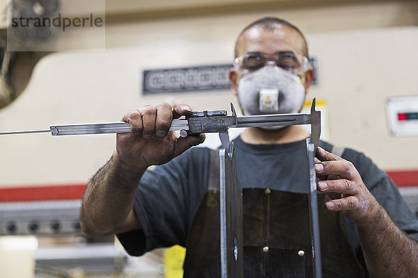 Spanischer Arbeiter misst Metall mit einem Messschieber in einer Fabrik