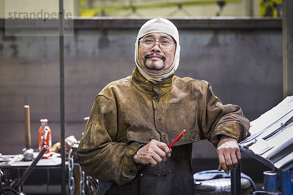 Lächelnder asiatischer Arbeiter mit Kapuze posiert in einer Fabrik