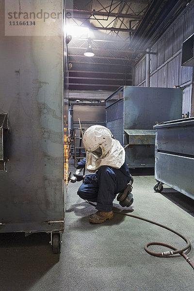Kaukasischer Arbeiter schleift Metallbehälter in einer Fabrik