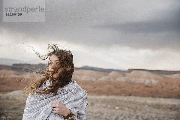 Eine Frau mit langen Haaren  die im Wind weht und in einer Wüstenlandschaft steht.