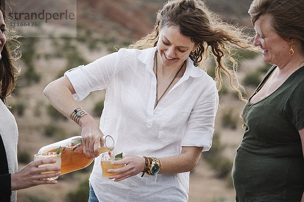 Drei Frauen stehen in einer Wüstenlandschaft und trinken etwas.