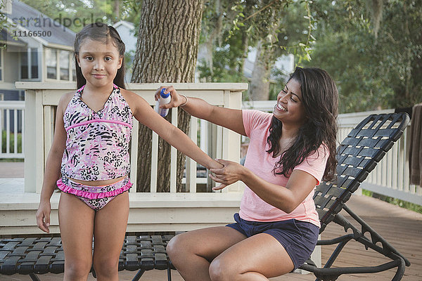 Hispanische Mutter sprüht Sonnenschutzmittel auf den Arm ihrer Tochter