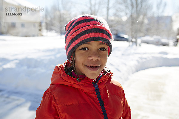 Lächelndes gemischtrassiges Mädchen mit Hut und Mantel im Winter