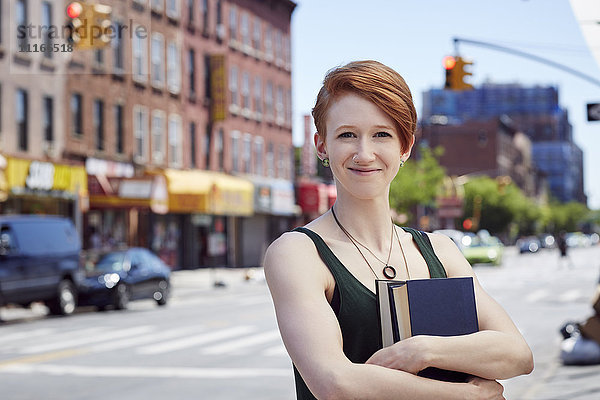 Weiße Frau trägt Bücher auf dem Bürgersteig der Stadt