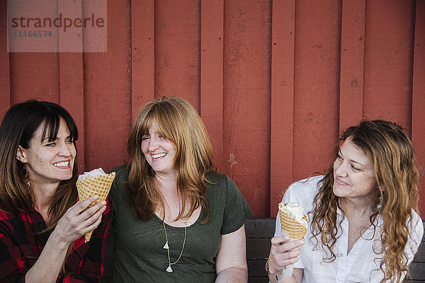 Drei Frauen sitzen auf einer Bank und essen Eiscreme.