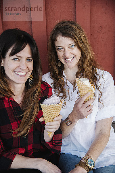 Zwei Frauen sitzen auf einer Bank und essen Eiscreme.