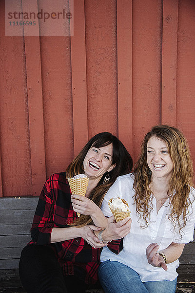 Zwei Frauen sitzen auf einer Bank und essen Eiscreme.