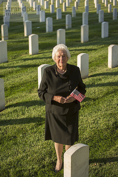Kaukasische Witwe hält amerikanische Flagge auf dem Friedhof