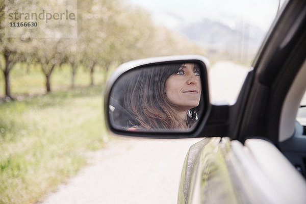 Frau im Auto auf einer Autofahrt  Spiegelung im Seitenspiegel gesehen.