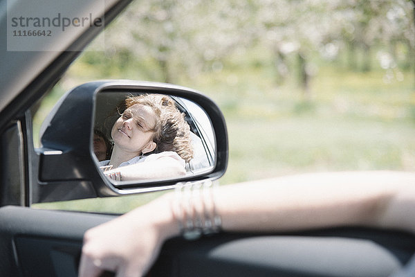 Frau in einem Auto auf einer Autofahrt  Blick aus dem Fenster  Spiegelung im Seitenspiegel.