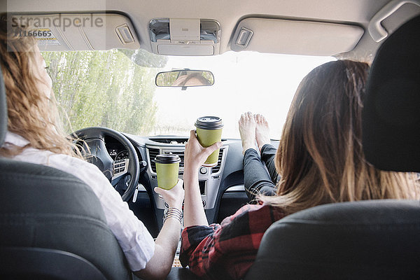 Zwei Frauen in einem Auto auf einer Autoreise  barfuß auf dem Armaturenbrett. Blick von hinten.