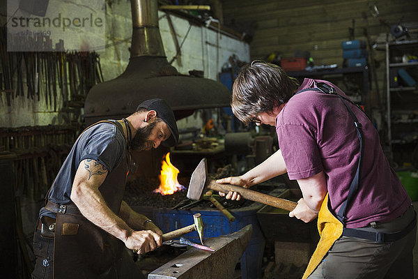 Zwei Schmiede hämmern in einer Werkstatt ein Stück Metall auf einen Amboss
