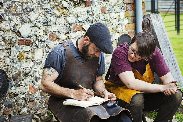 Zwei Männer mit Schürzen  die in ein Notizbuch schrieben  saßen in einem Garten.