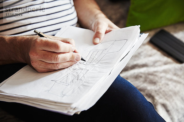 Ein Mann  der mit einer Feder sitzt und Skizzen zeichnet  ein Designer bei der Arbeit.