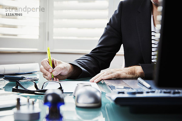 Ein Mann sitzt an einem Schreibtisch in einem Büro und hält einen Stift in der Hand.