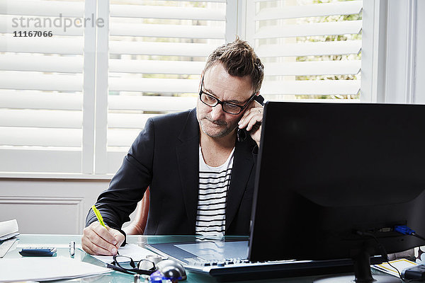 Ein Mann sitzt in einem Büro am Schreibtisch  einen Stift in der Hand  am Telefon.