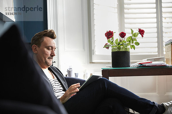 Mann sitzt in einem Büro und benutzt sein Mobiltelefon  eine Vase mit roten Rosen auf einem Schreibtisch.