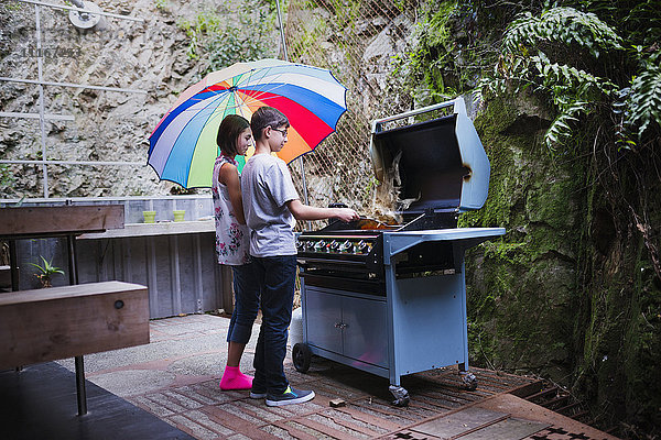 Mixed Race Bruder und Schwester kochen auf der Terrasse Grill unter Sonnenschirm