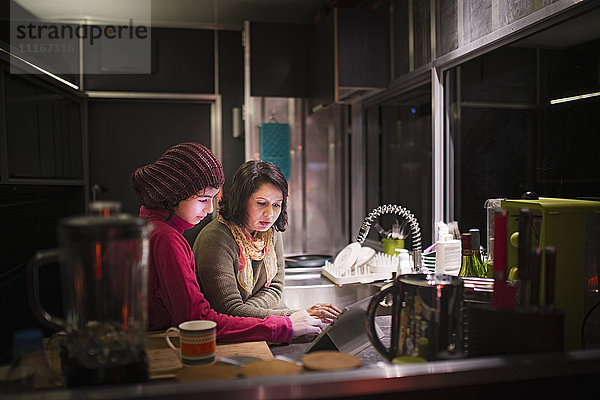 Mutter und Tochter benutzen nachts ein digitales Tablet in der Küche