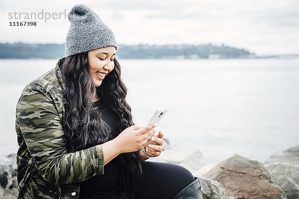 Lächelnde Mixed Race Frau texting auf Handy in der Nähe von Meer