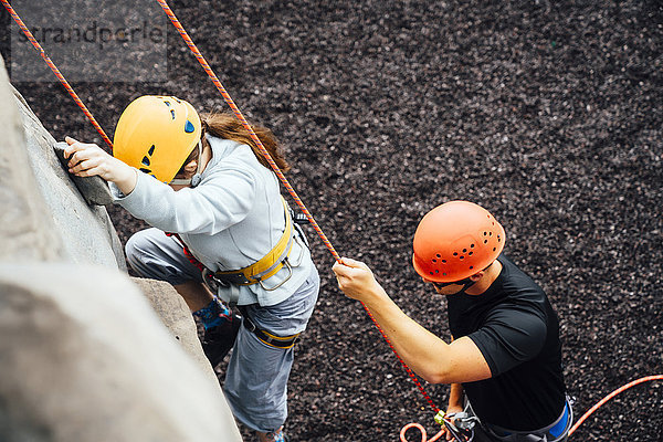 Kaukasischer Mann hält Seil für Frau beim Klettern an der Kletterwand