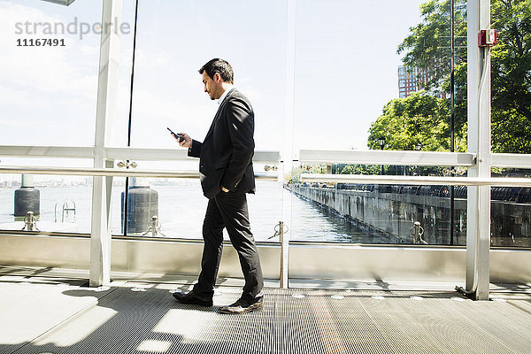 Geschäftsmann in einem grauen Anzug  der im Freien steht und sein Mobiltelefon benutzt.