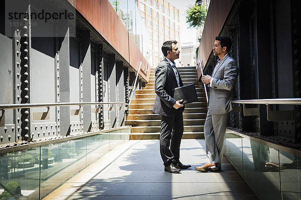 Zwei Geschäftsleute in grauen Anzügen stehen im Freien und unterhalten sich miteinander.