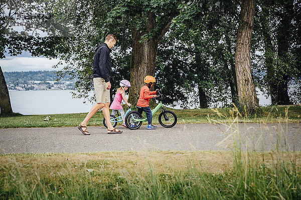 Vater beobachtet Tochter und Sohn beim Fahrradfahren